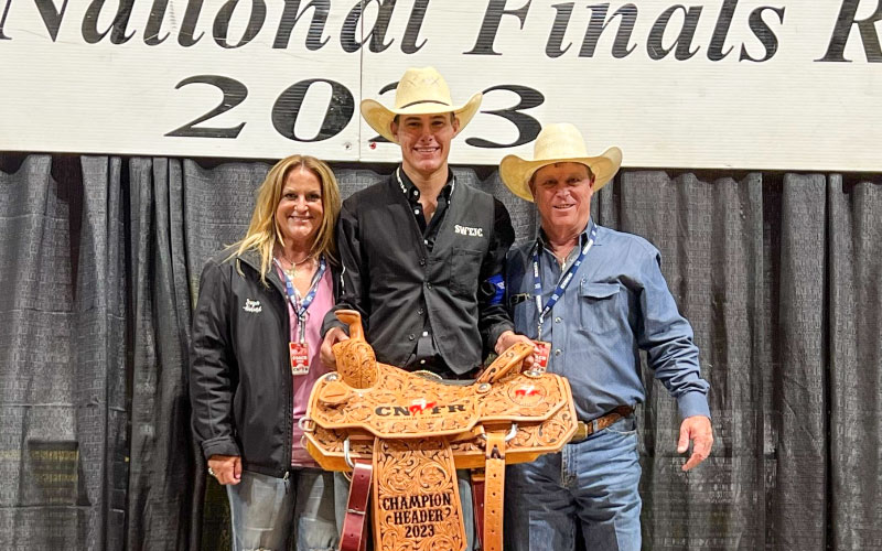 Slade Wood (center) accepts a custom champion saddle during the CNFR with coach Joey Almand (right) and his wife Sugar Almand.